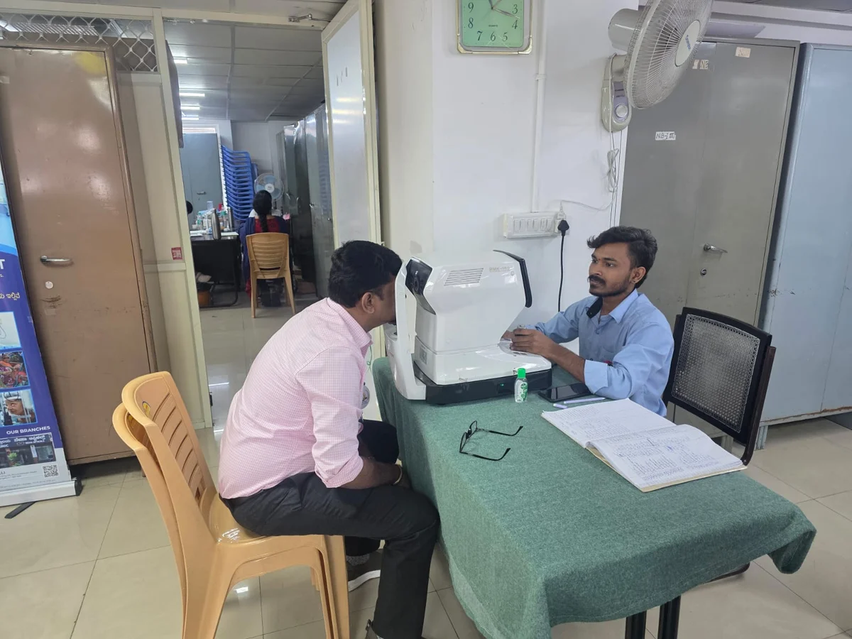 Optometrist operating an autorefractometer machine for computerized eye screening at a community camp